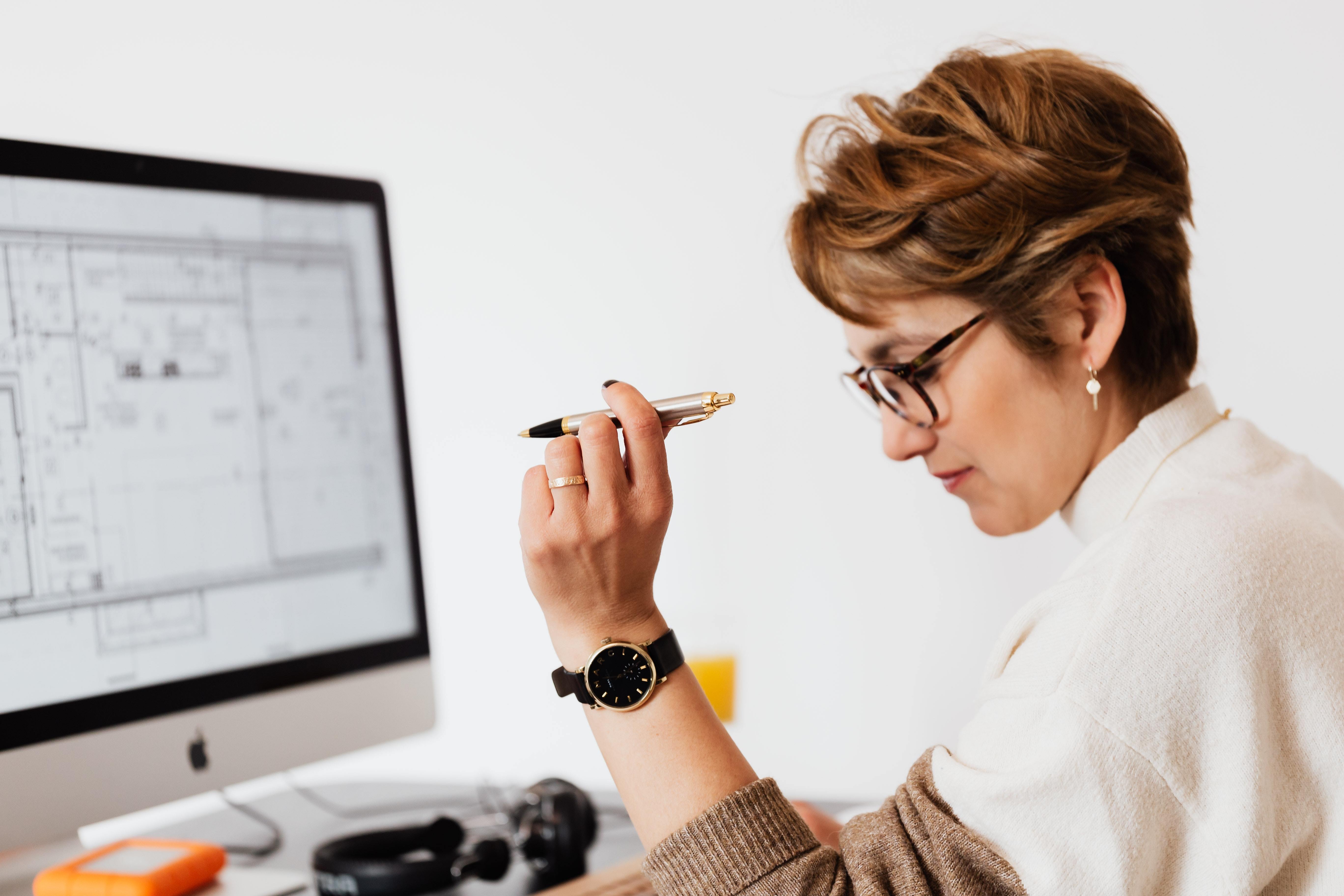 Eine Frau hält einen Stift und schaut auf einen Computer mit Bauplan, vermutlich bei der Erstellung von Sicherheitskonzepten für Limburger Sicherheitstechnik.