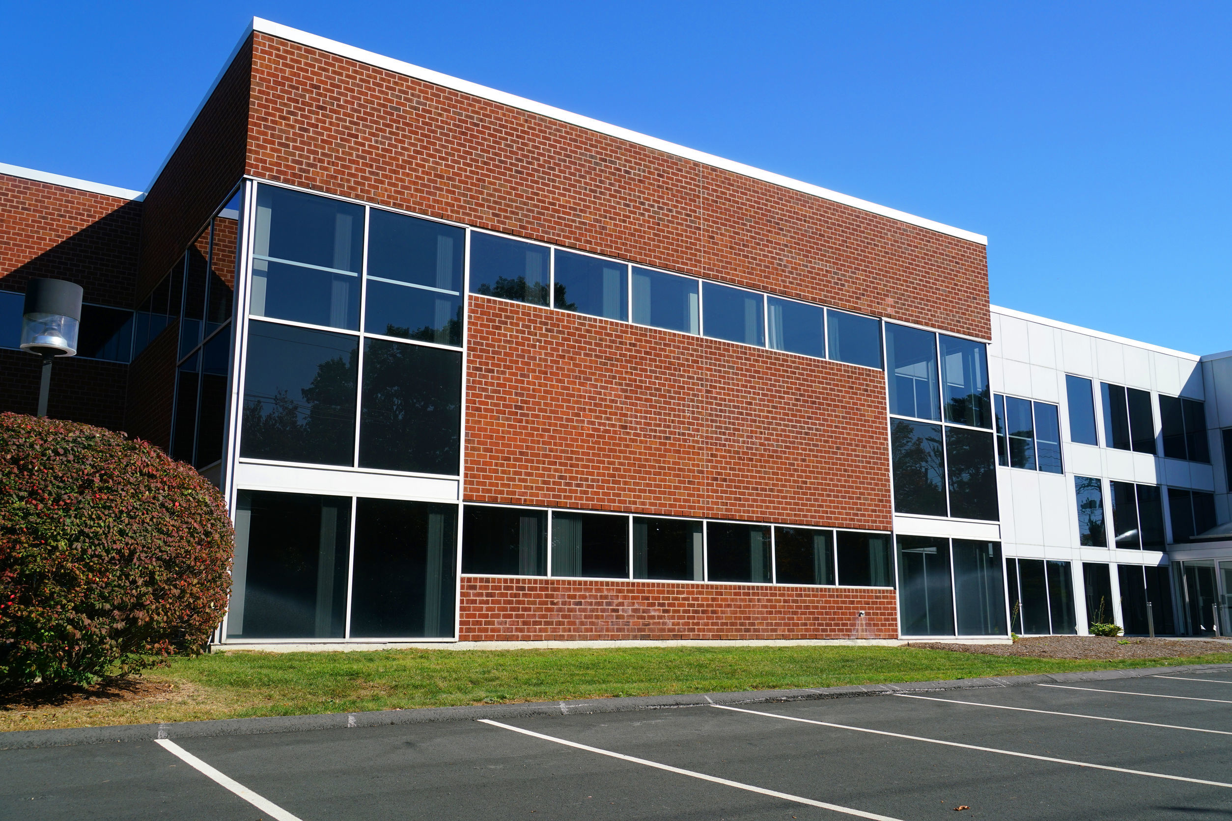 Modernes Bürogebäude mit roter Ziegelmauer und großen Glasfenstern, repräsentativ für die Niederlassung der Limburger Sicherheitstechnik, einem VdS-zertifizierten Sicherheitsdienstleister, der auf Risikominimierung und Sicherheitstechnik spezialisiert ist.