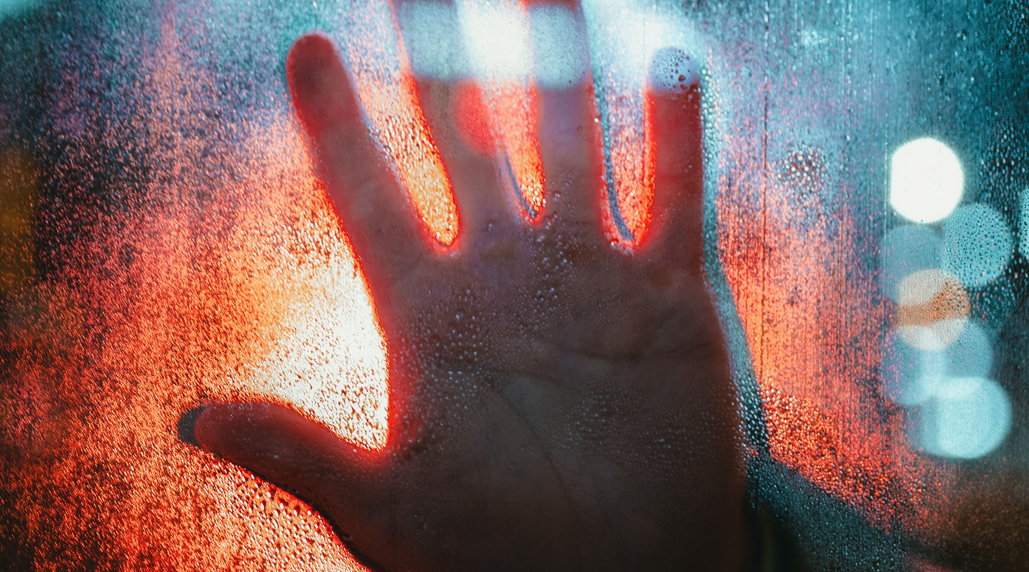 Hand auf beschlagenem Glas mit roten und blauen Lichtern, symbolisierend Sicherheitstechnik wie Zutrittskontrolle und Überwachung.