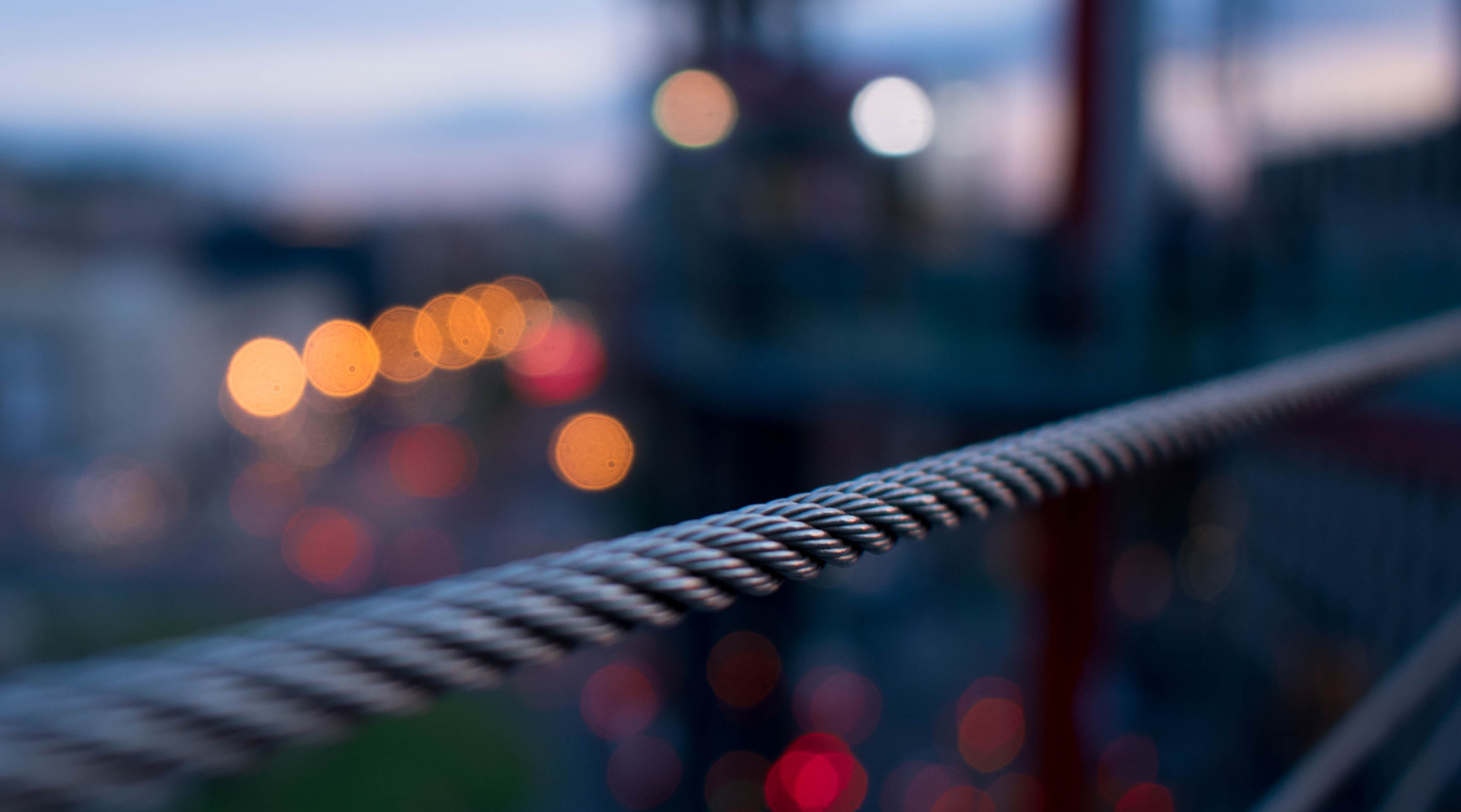 Gedrehtes Metallkabel im Vordergrund mit verschwommenen Abendstadtlights, repräsentierend Sicherheitsinfrastruktur und städtische Sicherheit.