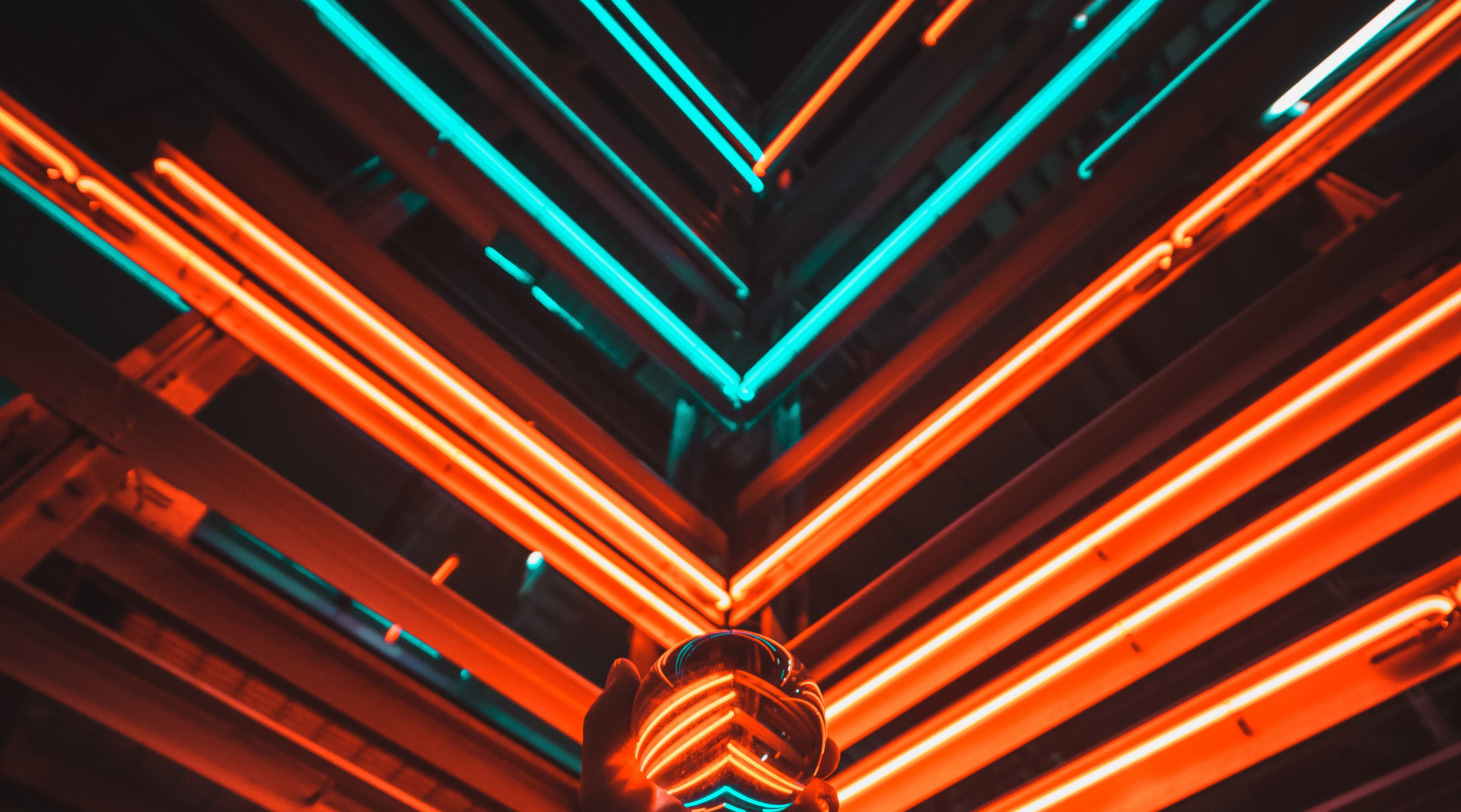 Neonbeleuchtung in Orange und Türkis mit geometrischen Mustern, Hand hält eine Kristallkugel, die die Lichter reflektiert – symbolisiert moderne Sicherheitstechnik und visuelle Überwachung.