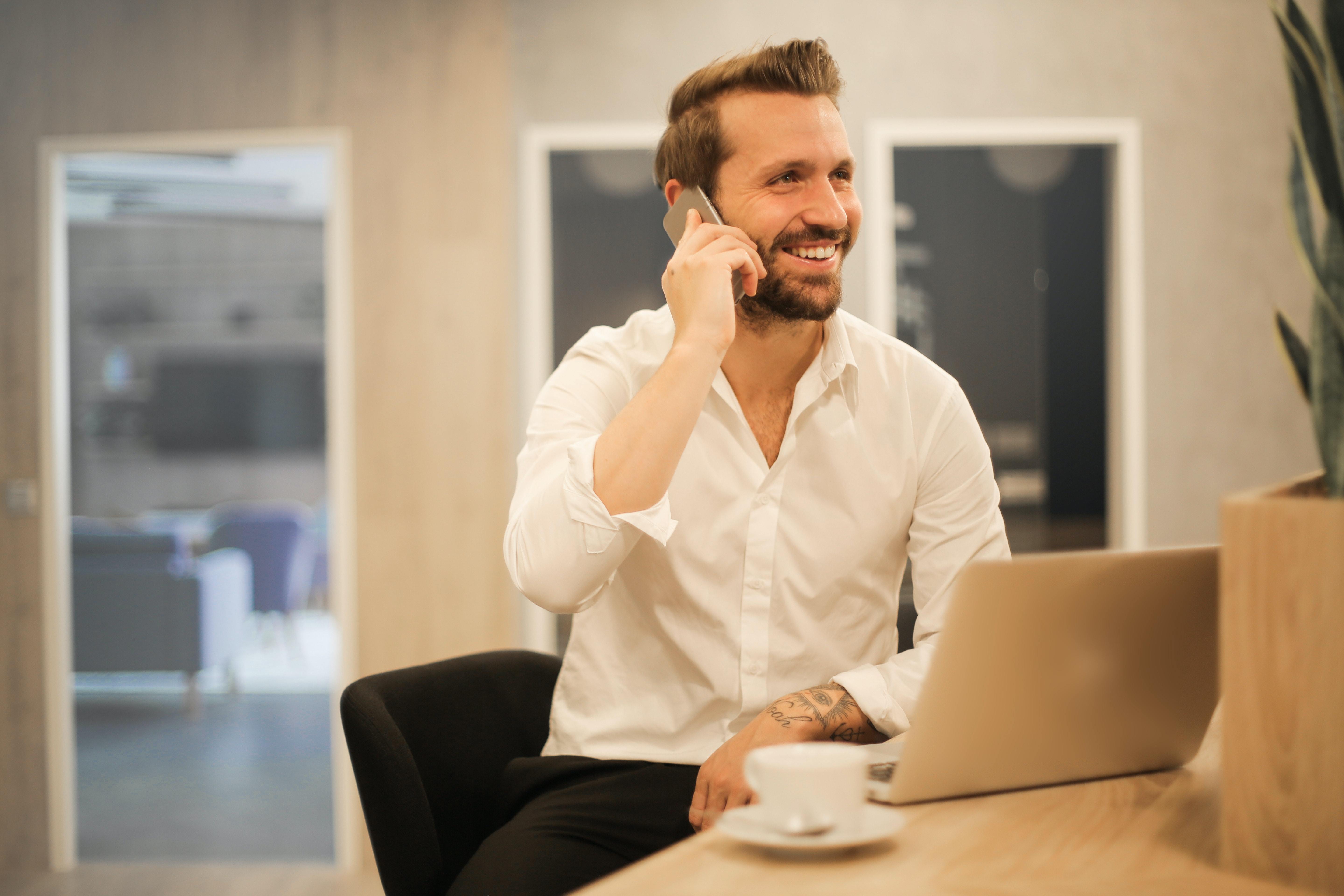 Ein Mann in einem weißen Hemd telefoniert am Schreibtisch mit Laptop und Kaffeetasse in einem modernen Büro, das die professionelle Arbeitsumgebung von Limburger Sicherheitstechnik widerspiegelt.