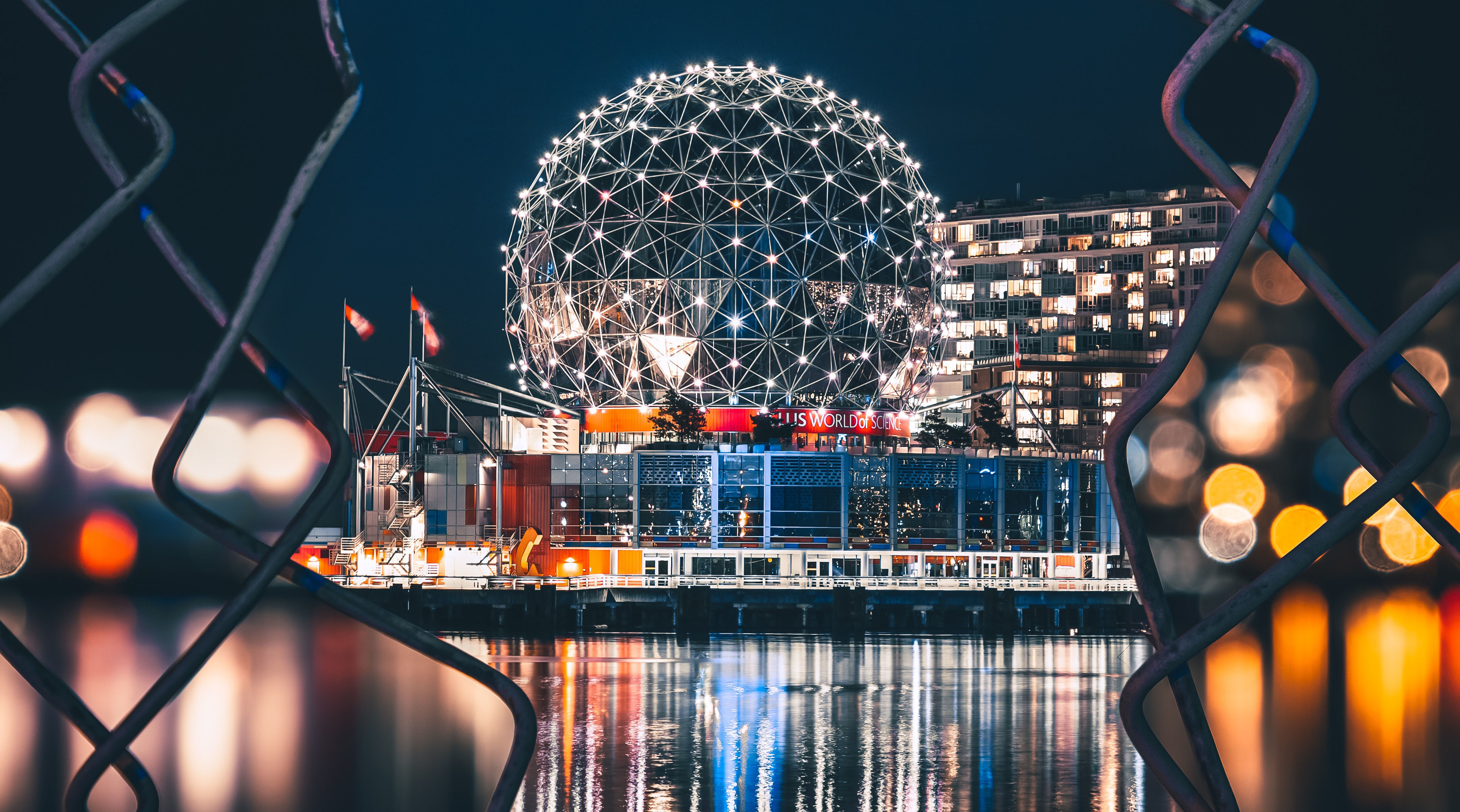 Nachtansicht des Telus World of Science in Vancouver: beleuchtete Kugelkonstruktion am Wasser, durch Zaun gerahmt – passend für Videouberwachungsthemen.