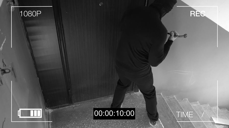 Sicherheitskamera-Aufnahme zeigt einen Einbrecher, der mit einem Werkzeug versucht, eine Tür zu öffnen – Beispiel für die Videoüberwachung von Limburger Sicherheitstechnik im Rahmen des Einbruchschutzes.