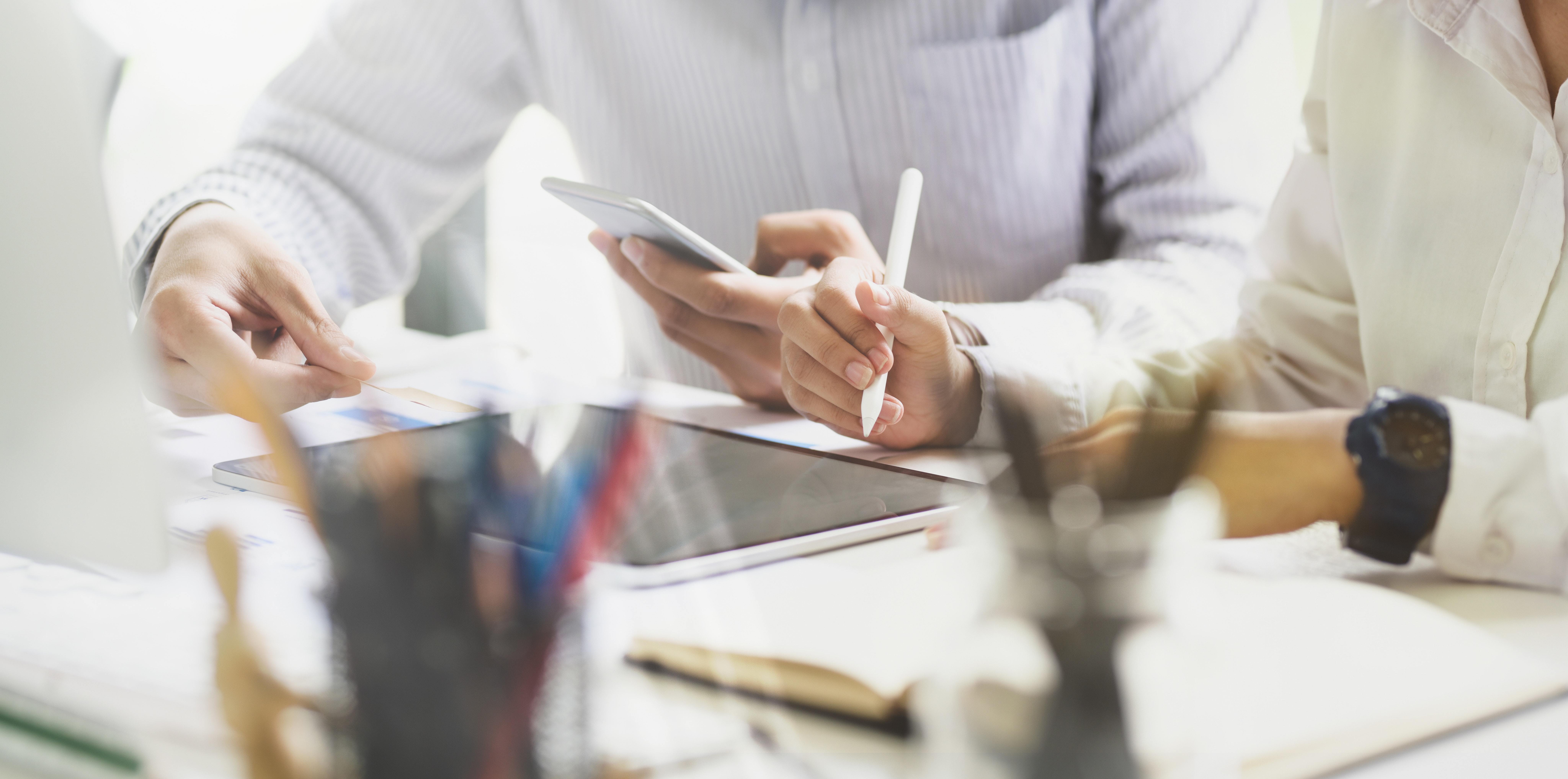 Zwei Personen arbeiten an einem Schreibtisch mit Smartphone, Stift und Tablets – ein typisches Szenario für die Zusammenarbeit in der Sicherheitsbranche, wie sie Limburger Sicherheitstechnik bei der Planung von Einbruch- und Brandmeldesystemen oder Videoüberwachung umsetzt.