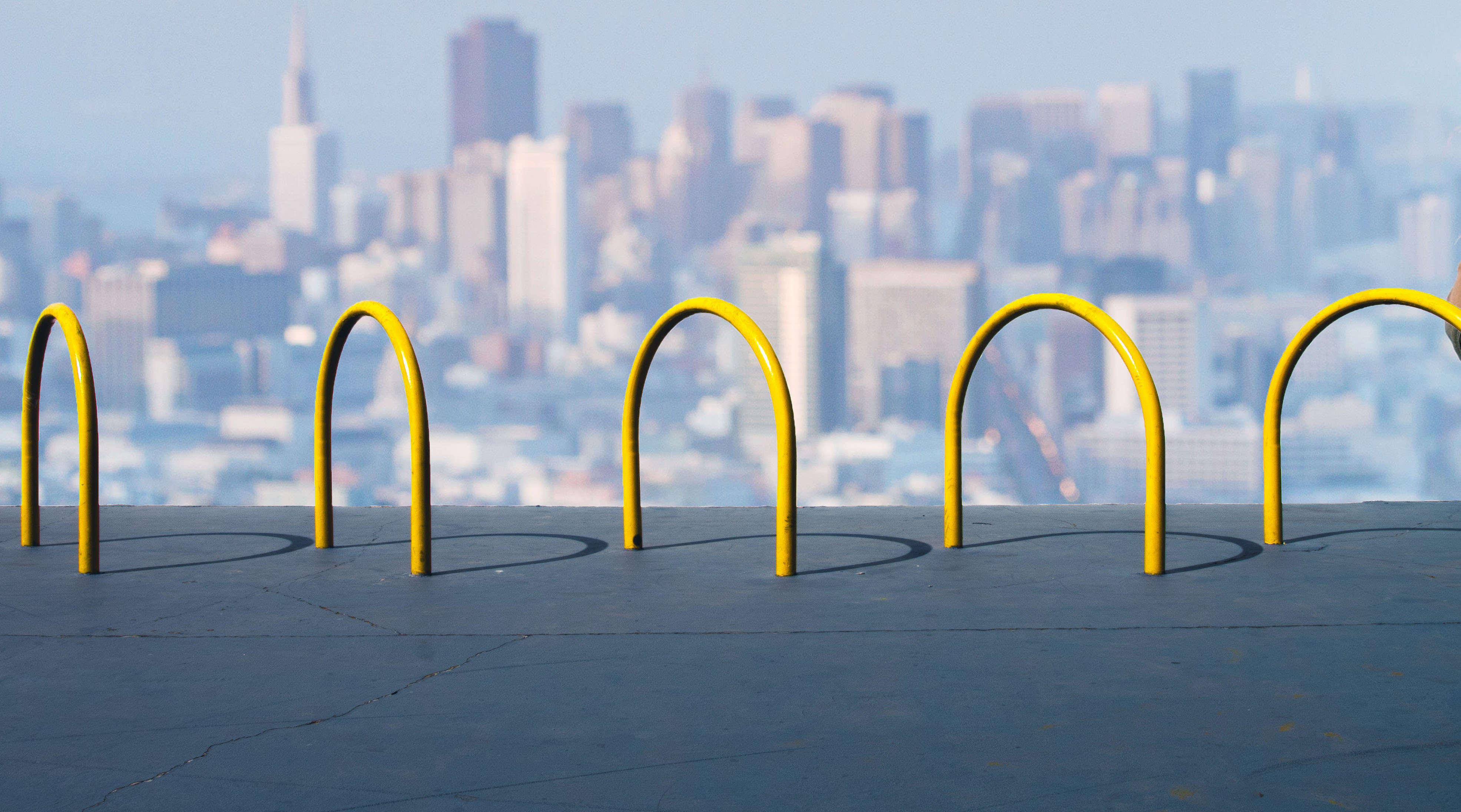 Gelbe Fahrradständer auf einer Dachterrasse mit Blick auf eine städtische Skyline im Hintergrund.
