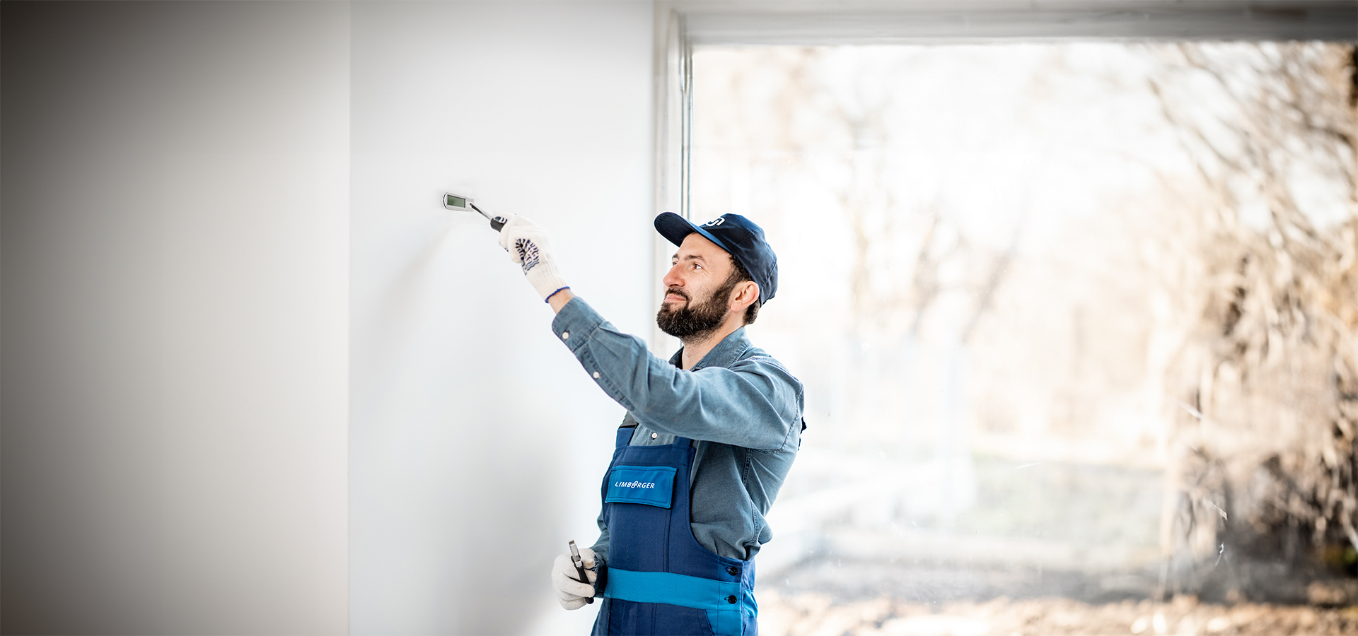Ein Mitarbeiter von Limburger Sicherheitstechnik streicht eine Wand mit einem Pinsel, während er an einem Sicherheitsprojekt arbeitet.