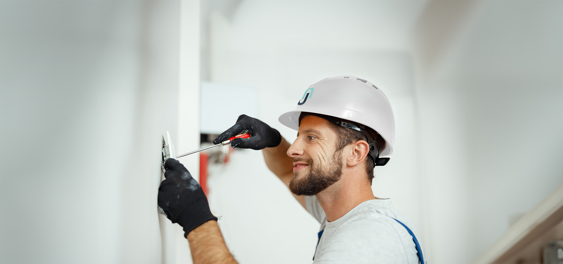 Ein Techniker mit Helm und Handschuhen arbeitet mit einem Schraubendreher an einer Wandmontage, vermutlich bei der Installation von Sicherheitstechnik.