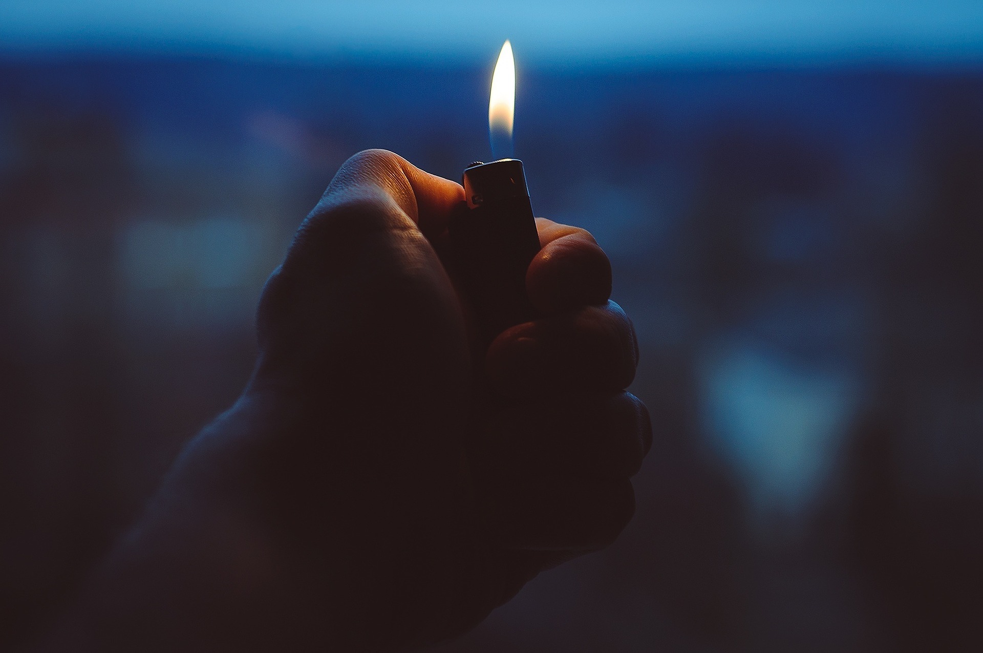 Hand hält ein brennendes Feuerzeug, das Brandgefahr symbolisiert und die Notwendigkeit von Brandmeldesystemen für die Sicherheitstechnik unterstreicht.