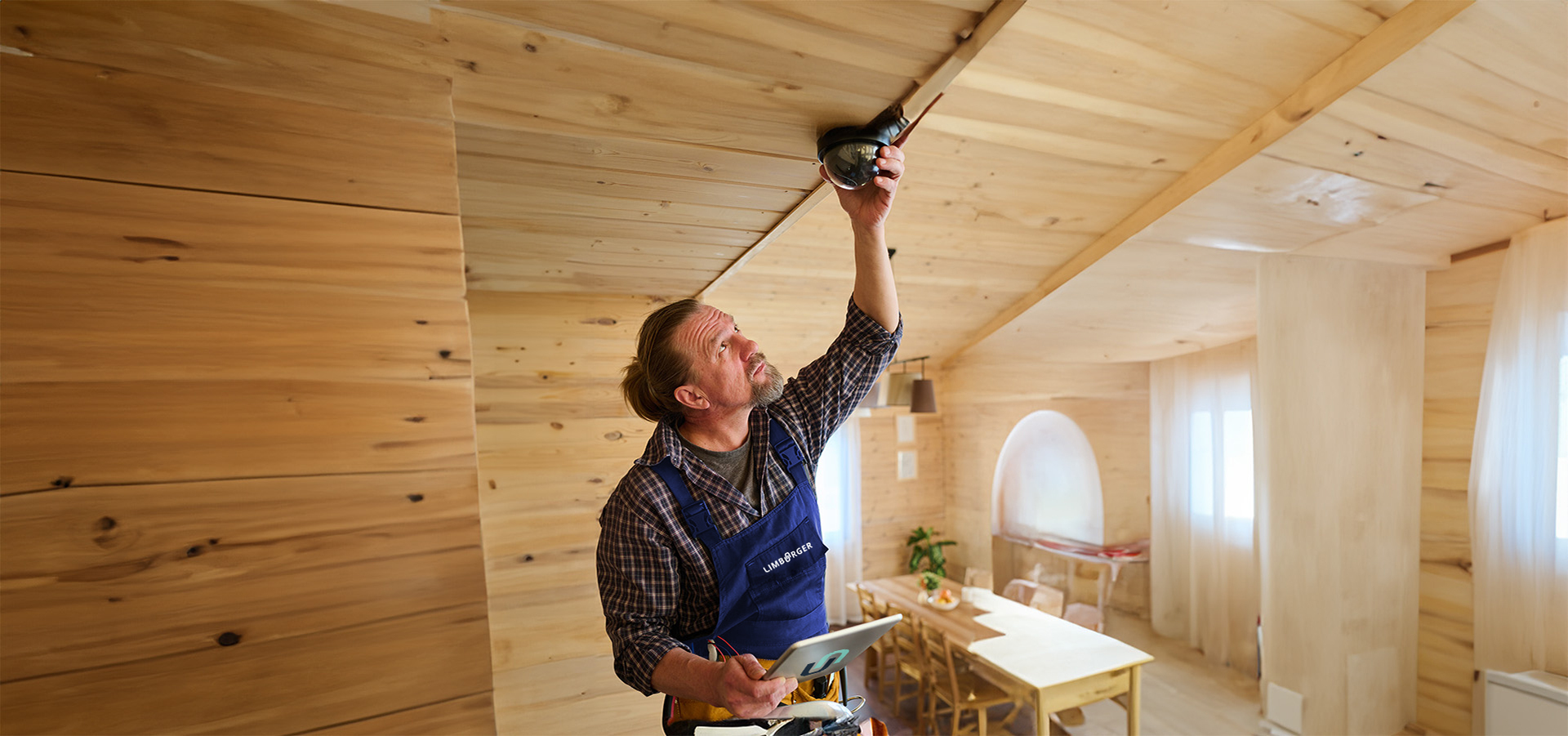 Ein Elektriker von Limburger Sicherheitstechnik installiert ein Deckengerät in einem holzverkleideten Raum, was die Expertise des Unternehmens in der Installation von Sicherheitstechnik unterstreicht.