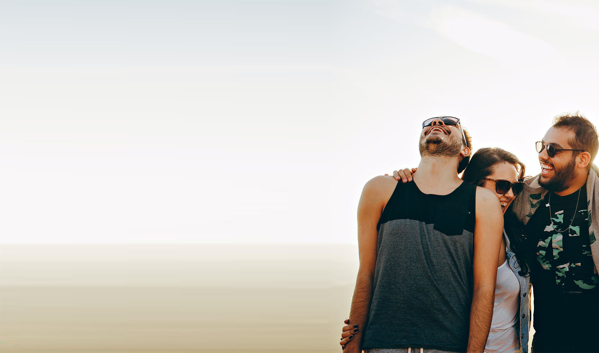 Zwei Männer und eine Frau stehen zusammen im Freien, lächeln und strahlen eine freundliche, entspannte Atmosphäre aus – ein Bild von Gemeinschaft und Freude.